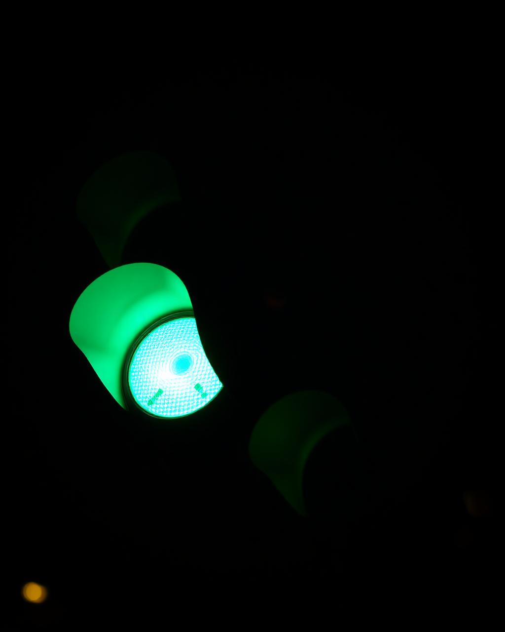 Illuminated green traffic light bulb against night sky