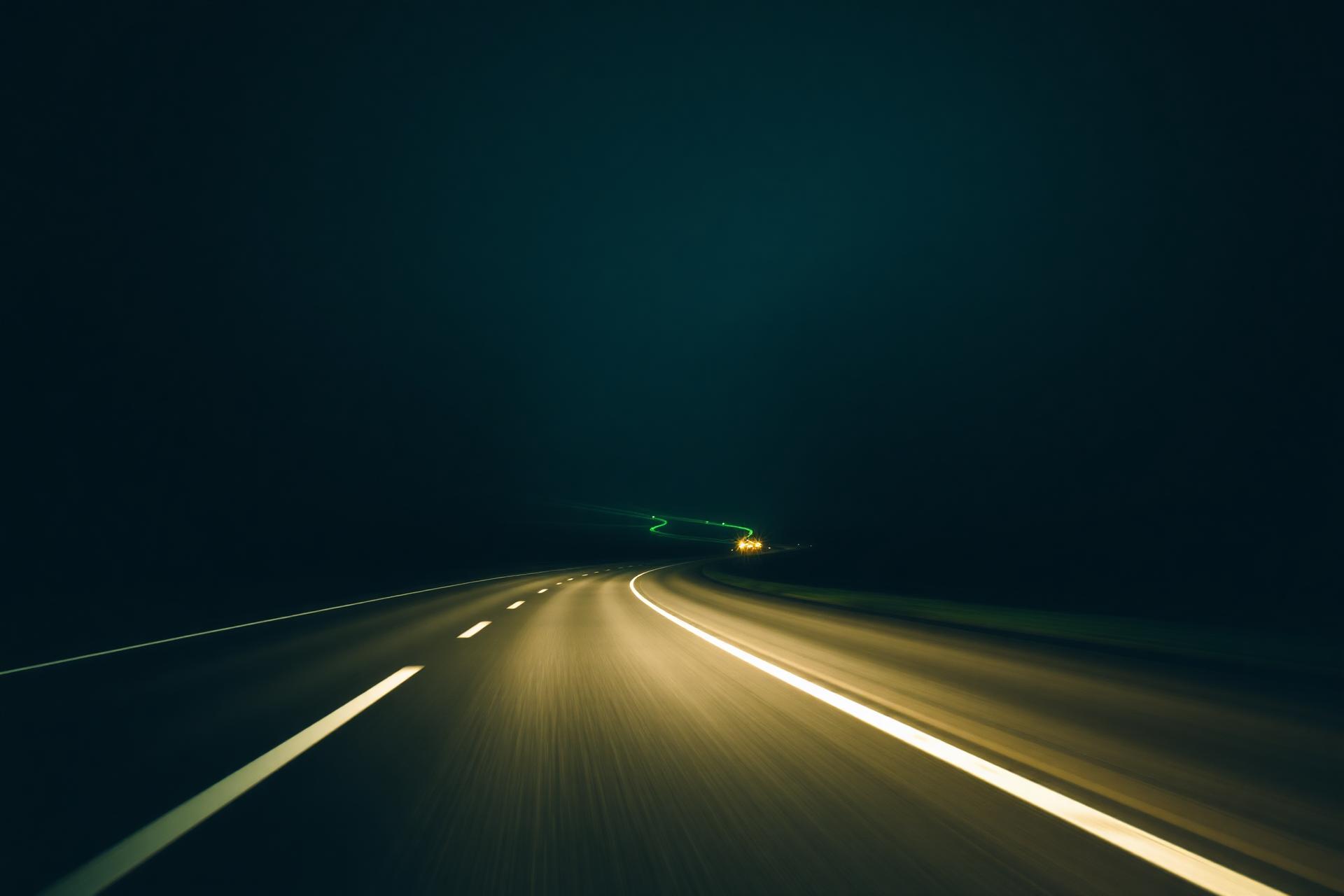Empty highway curving through the dark with green light streaks